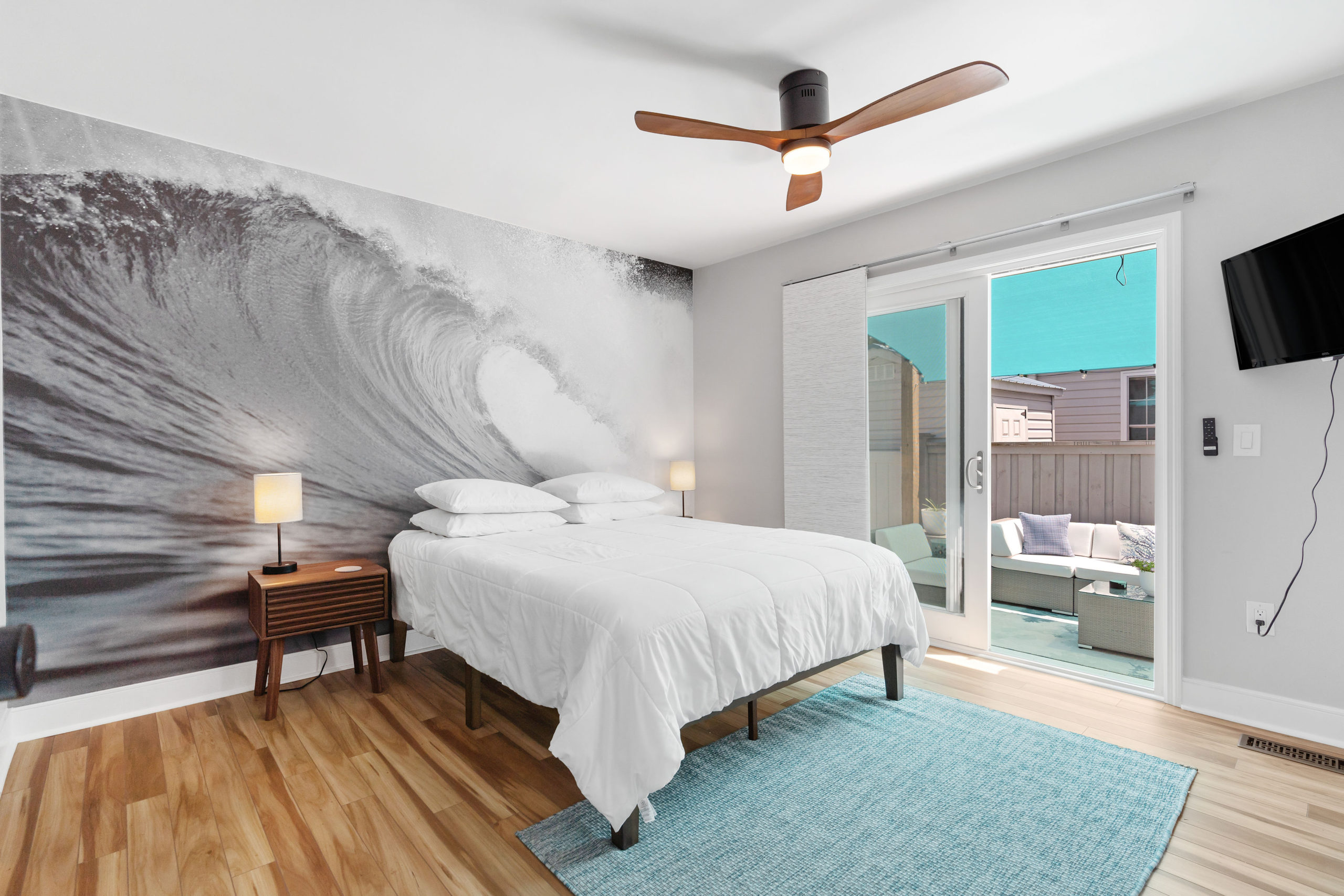 A view of the master bedroom called "The Boomer" and sliding doors leading to the outside shaded deck at CB Surf Cottage in Carolina Beach, NC.